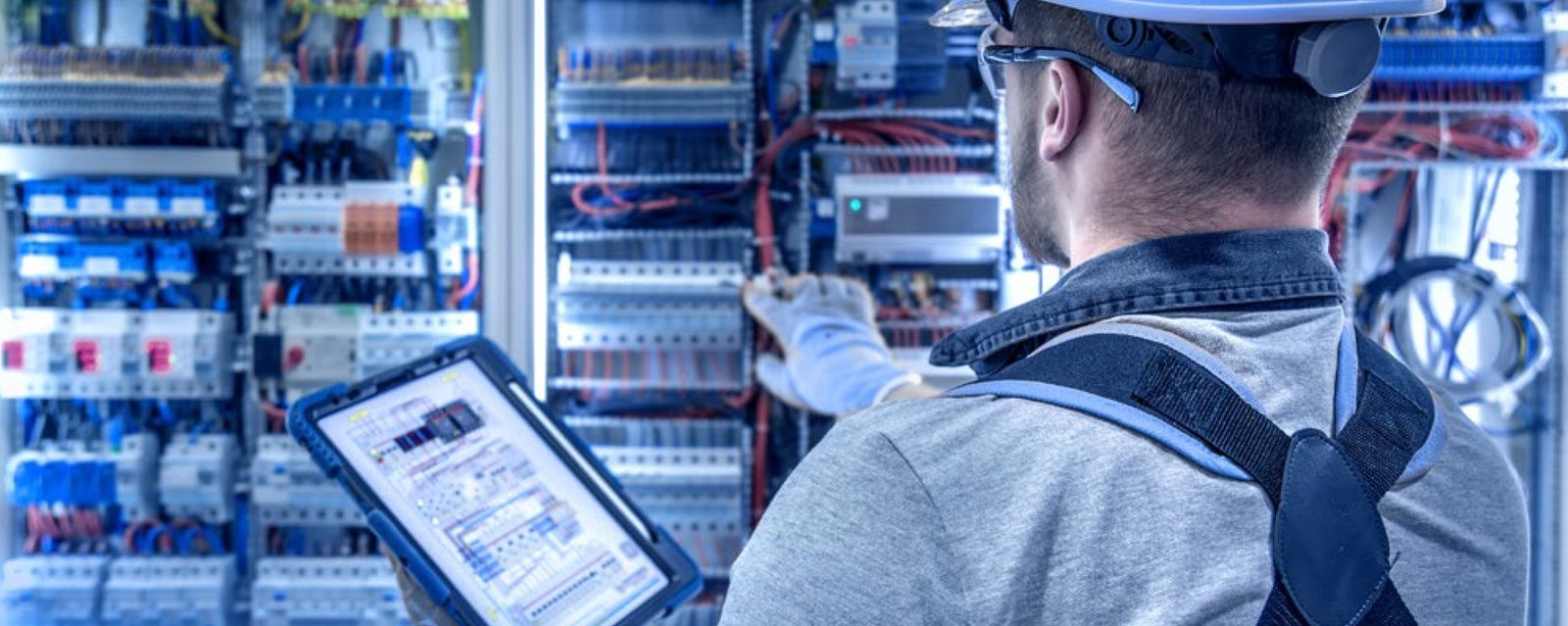 Tecnico con casco e tablet controlla lo schema di un quadro elettrico